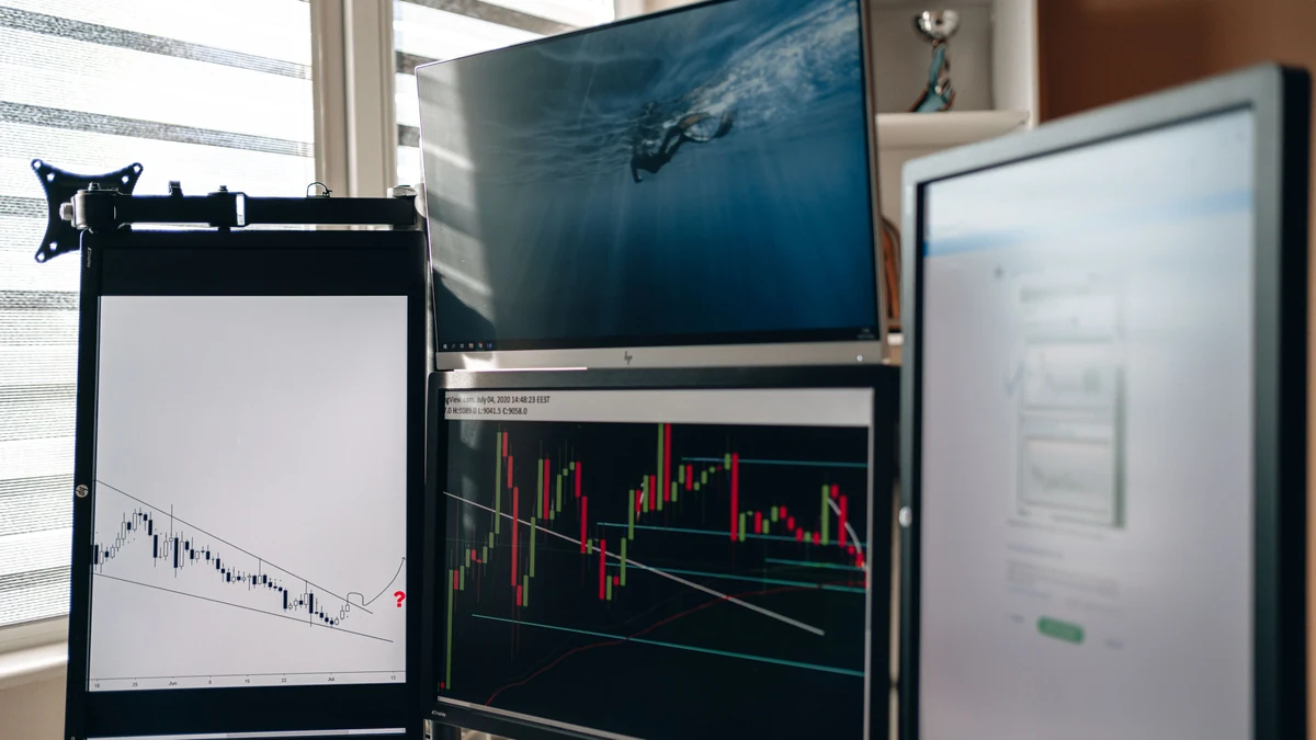 Computer workstation with multiple monitors, including screens displaying financial trading charts.
