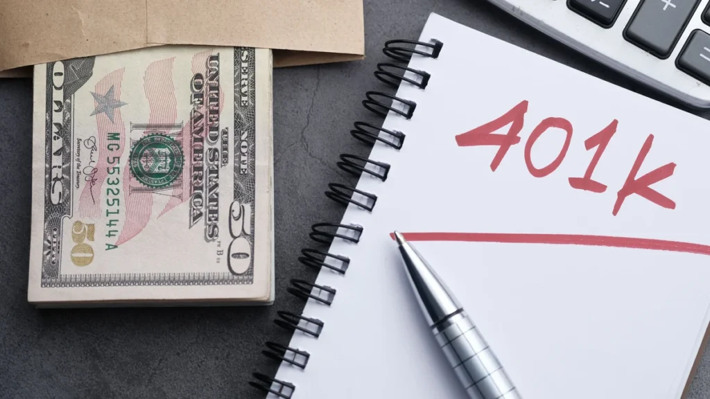 Cash, a calculator and a notebook labeled 401k on a desk.