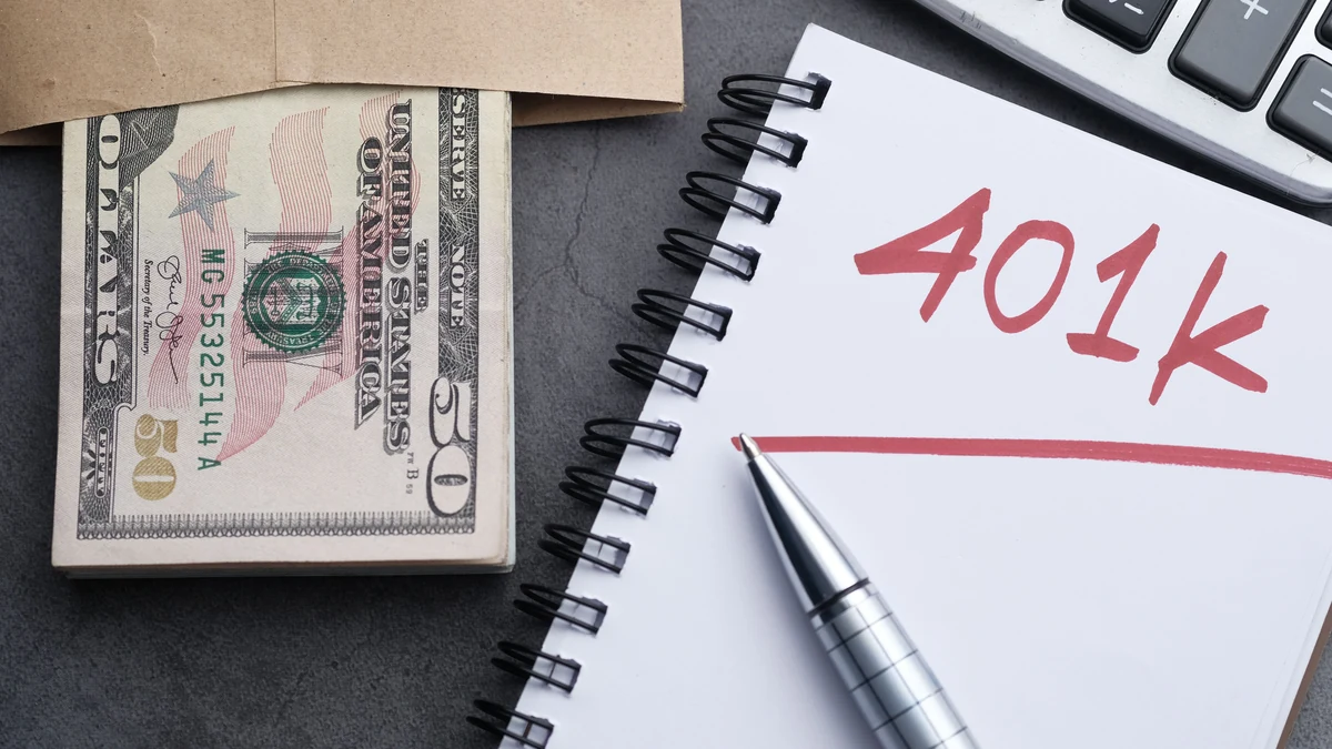 Cash, a calculator and a notebook labeled 401k on a desk.