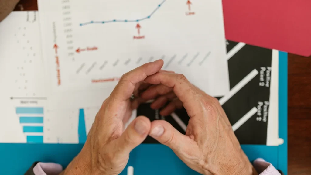 Hands over printed financial charts and graphs on a desk.