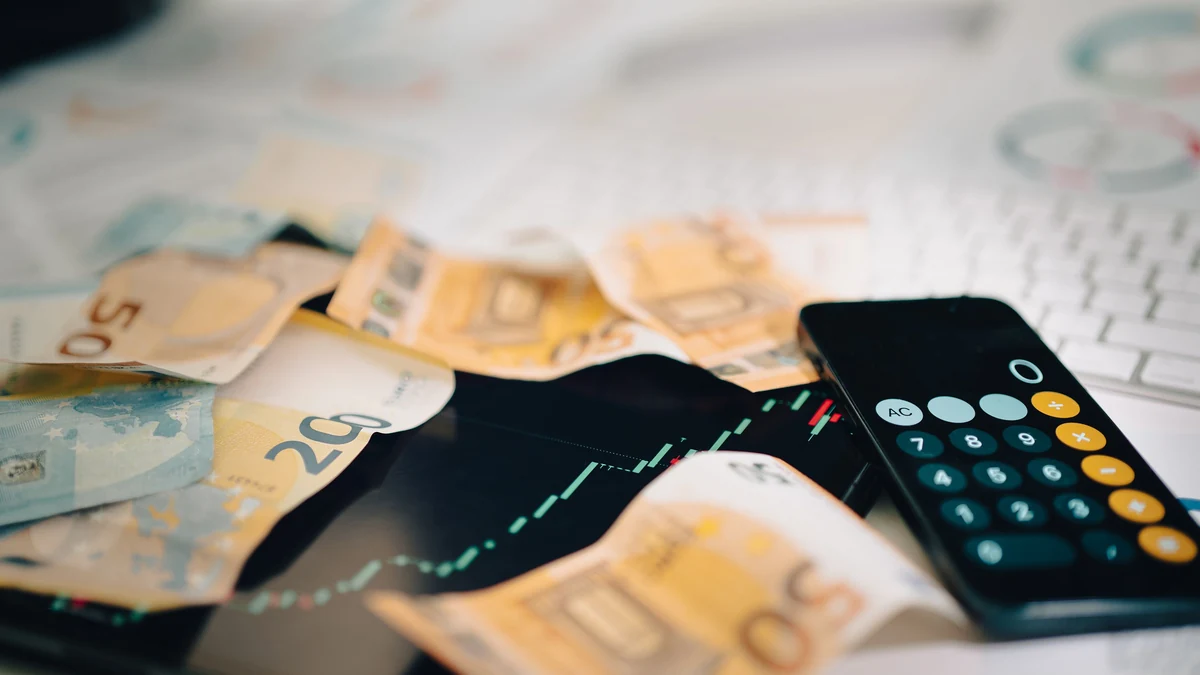 Euro banknotes scattered across a financial trading chart beside a calculator.