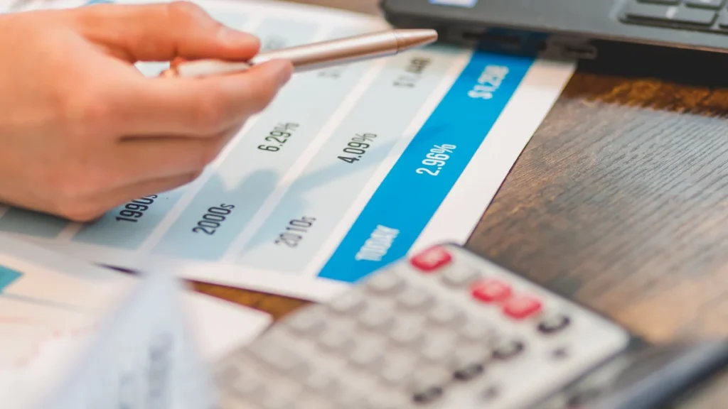 A hand pointing to interest-rate figures on a financial chart beside a calculator.