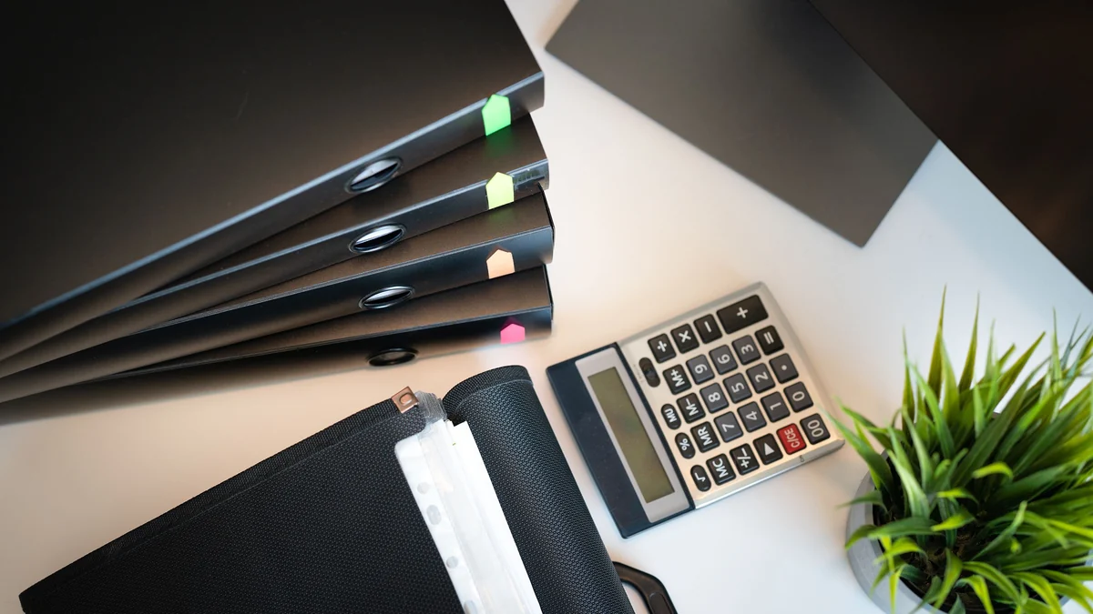 Top view of office folders, a calculator and a small plant on a desk.