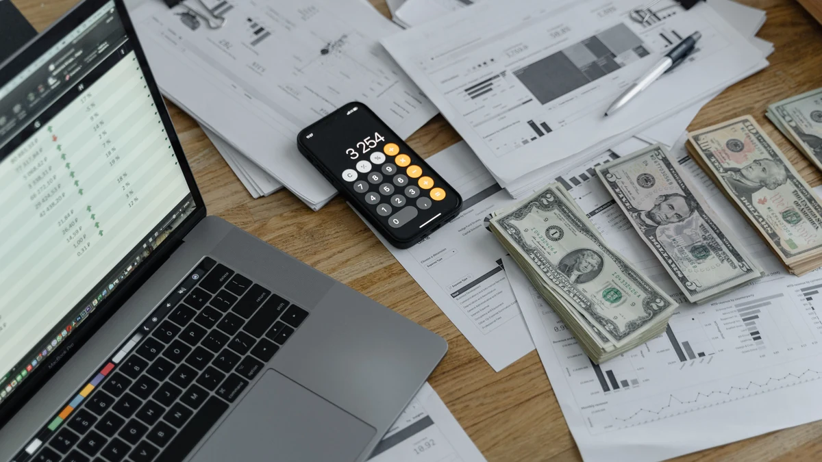 U.S. dollar bills, financial documents, a laptop and a calculator on a desk.