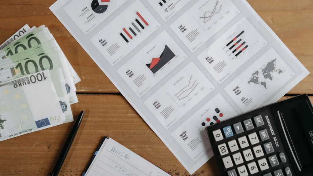 Euro banknotes, printed financial charts and a calculator on a wooden desk.