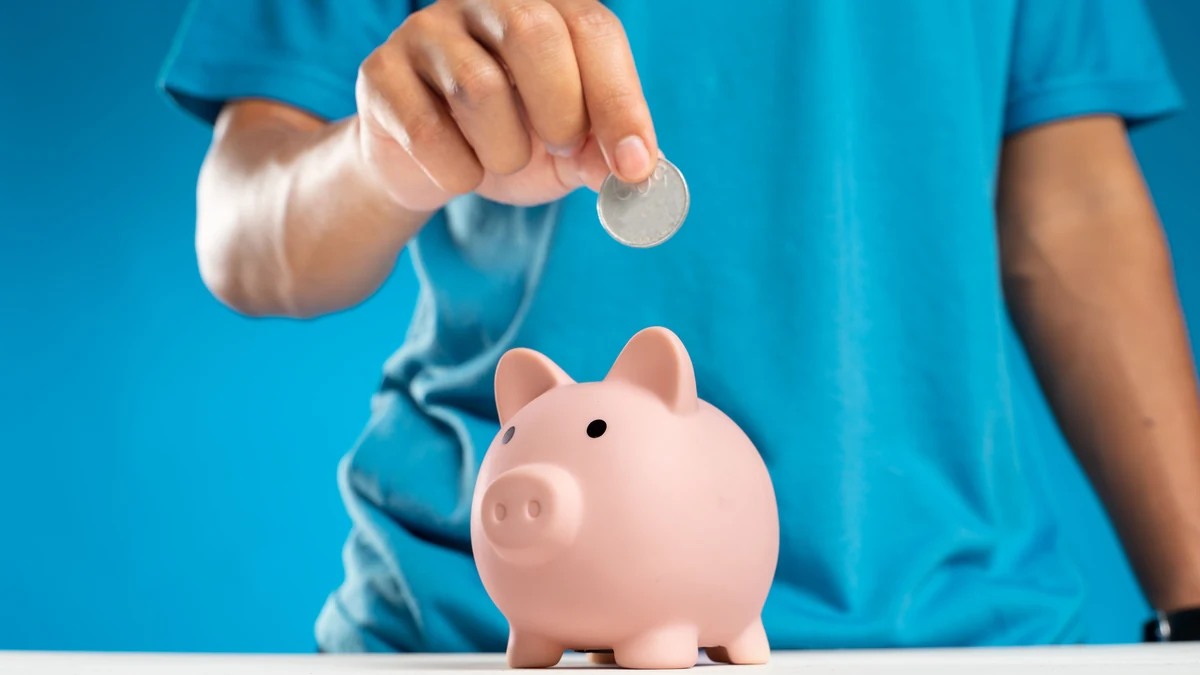 A person placing a coin into a pink piggy bank.