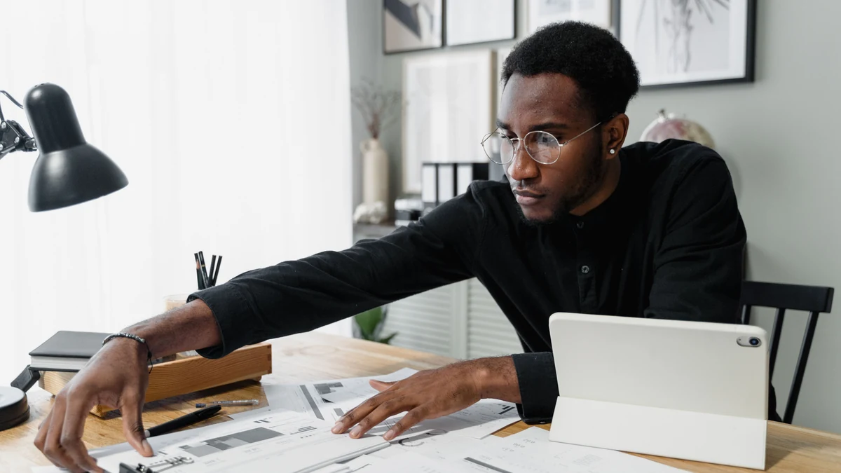 Business professional reviewing financial documents at a desk with a tablet.