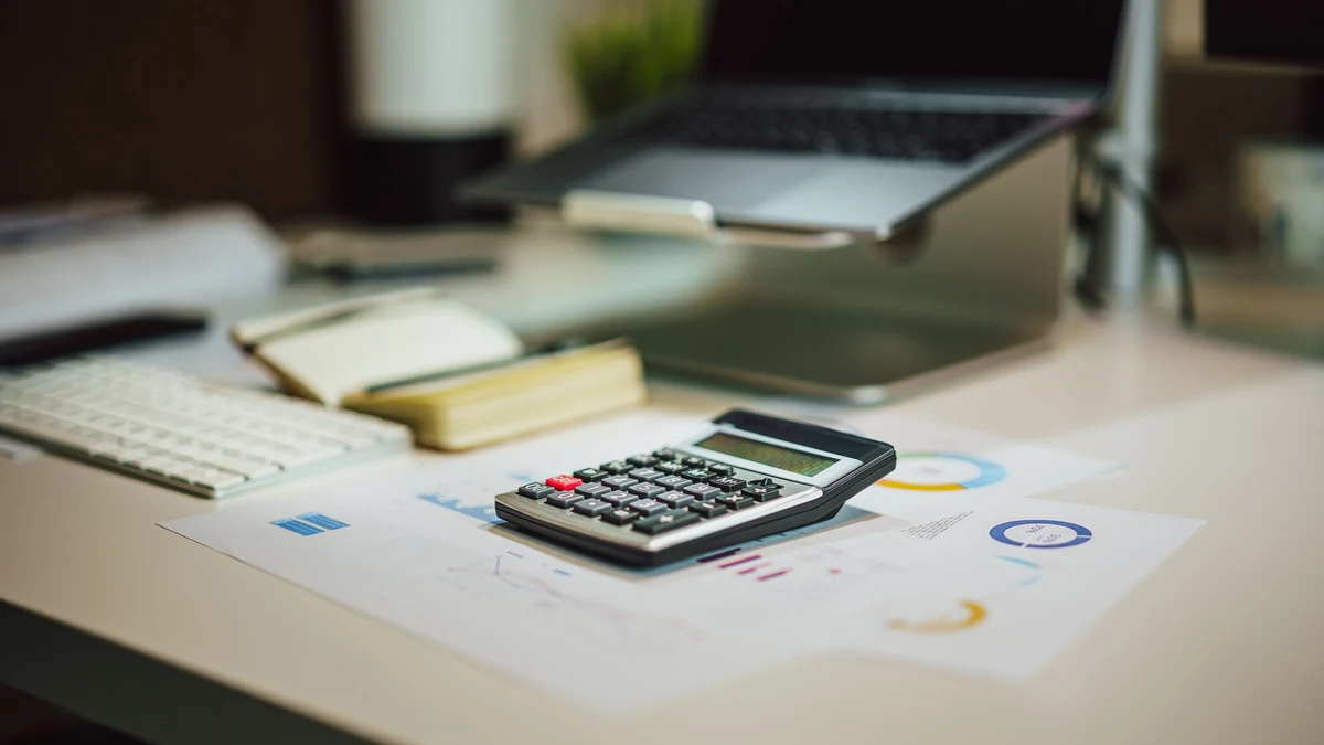 Calculator on financial documents beside a laptop and notebook.