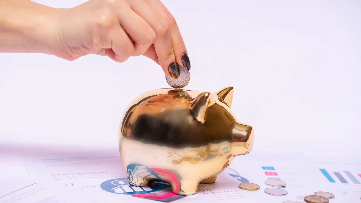 A hand placing a coin into a gold piggy bank on financial documents.