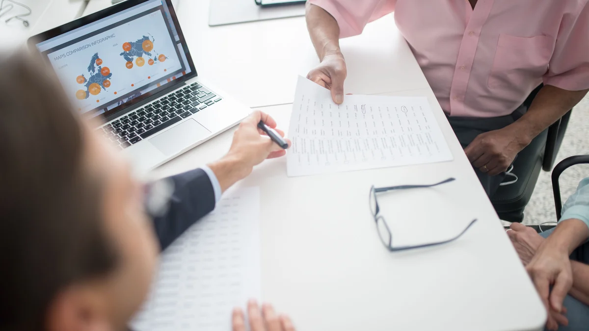 Older adults reviewing financial planning documents with an adviser at a desk.