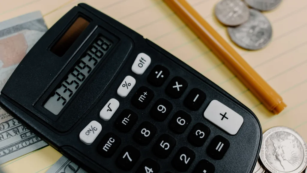 A black calculator surrounded by U.S. cash and coins on a notepad.