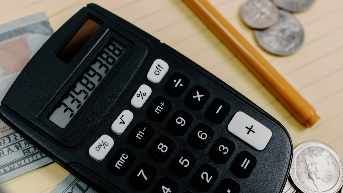 A black calculator surrounded by U.S. cash and coins on a notepad.
