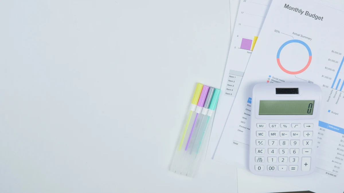 A calculator, monthly budget worksheet and pens arranged on a desk for financial planning.
