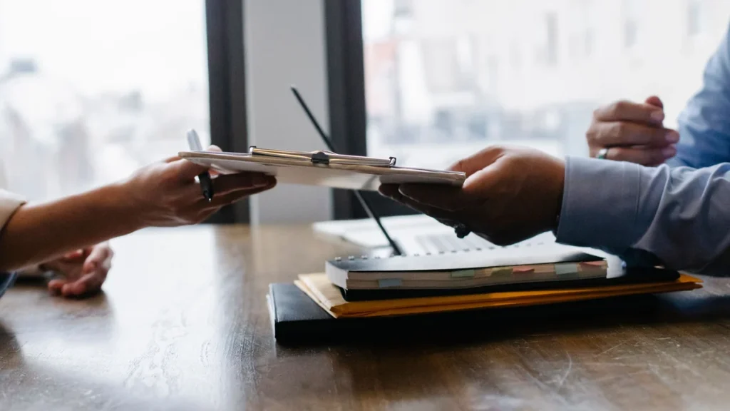 Hands exchanging a clipboard during a professional meeting at an office table.