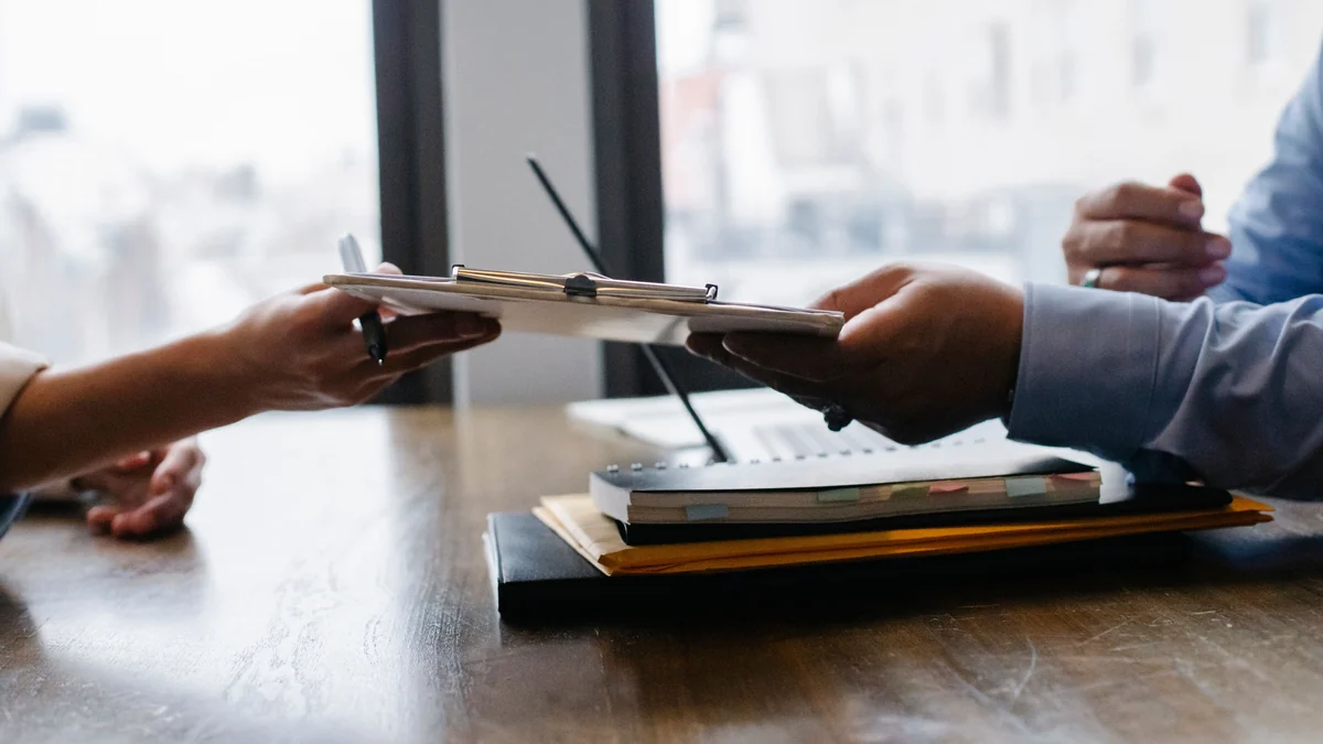 Hands exchanging a clipboard during a professional meeting at an office table.
