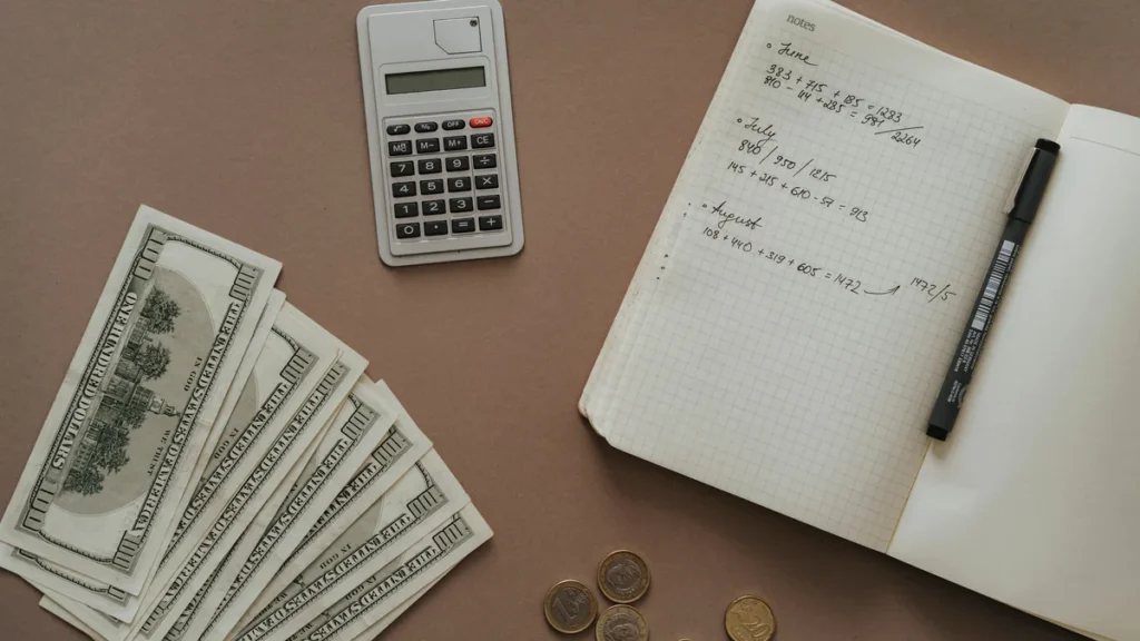Calculator, notebook, cash and coins arranged on a desk for financial planning.