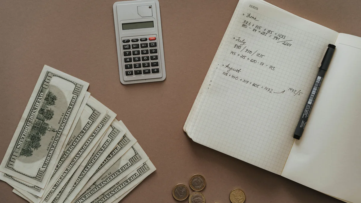 Calculator, notebook, cash and coins arranged on a desk for financial planning.