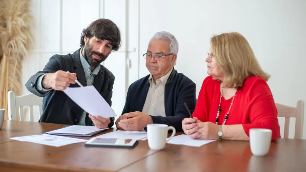 Older couple reviewing financial documents with an adviser at a table.