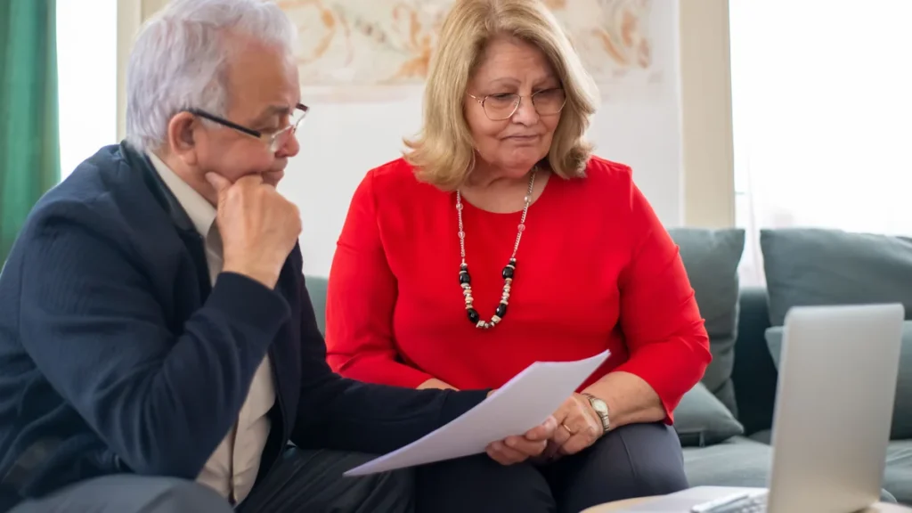 Older couple reviewing financial documents beside a laptop.