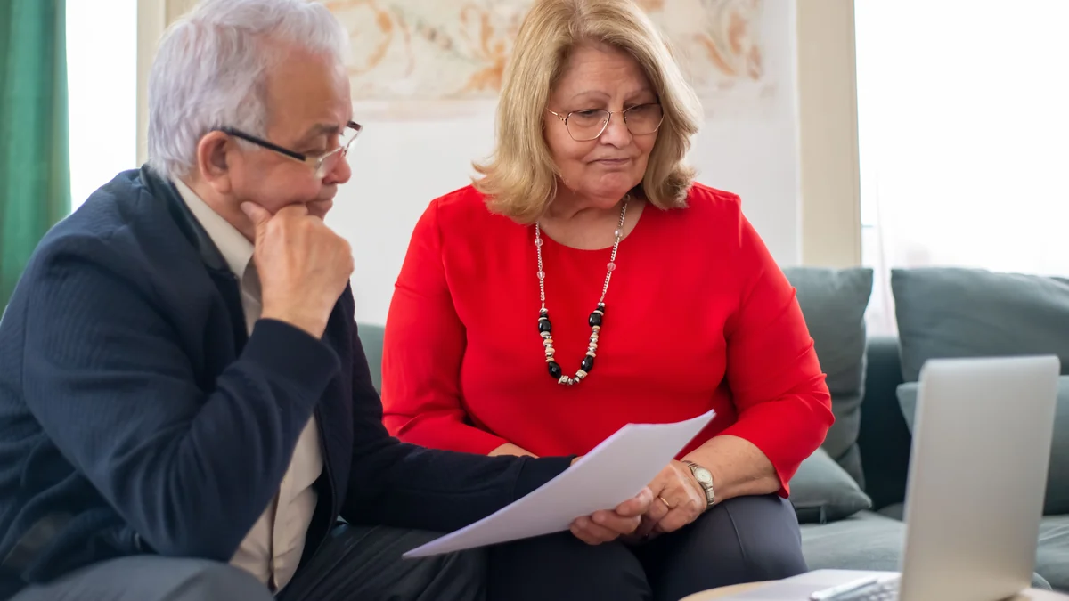 Older couple reviewing financial documents beside a laptop.