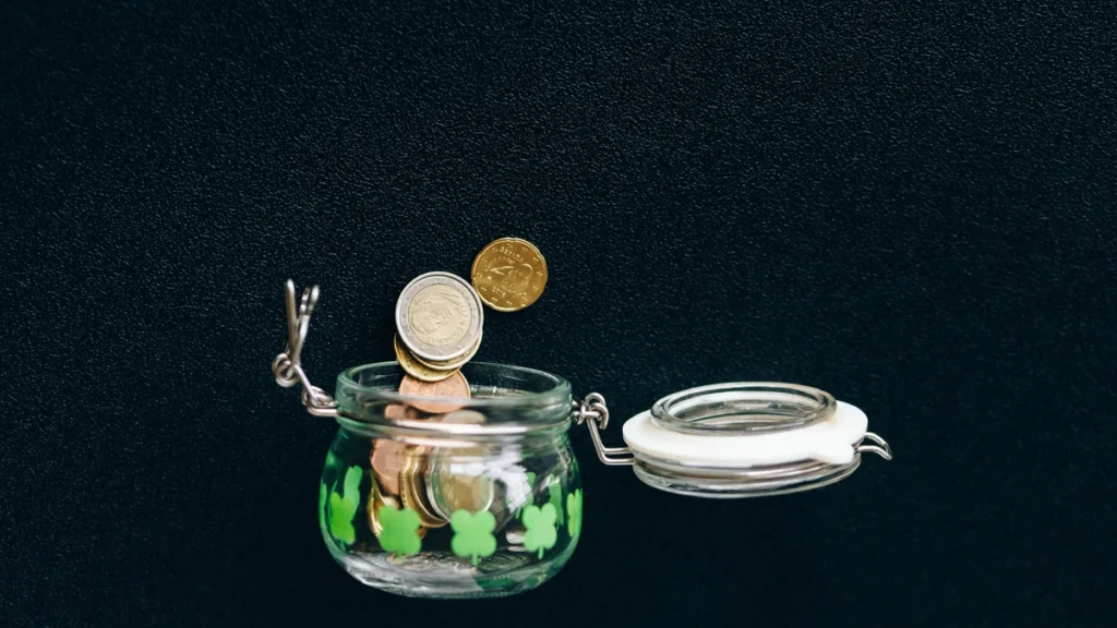 Coins falling into an open glass jar against a dark background.