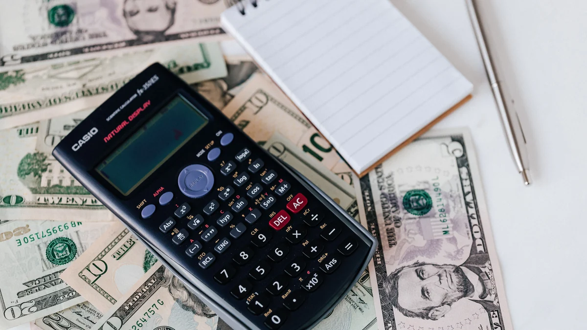 Calculator and notebook arranged over U.S. dollar bills on a desk.