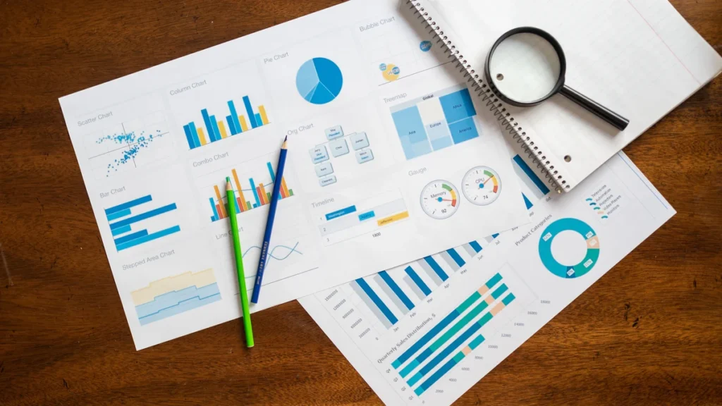 Financial charts, a magnifying glass and stationery arranged on a wooden desk.