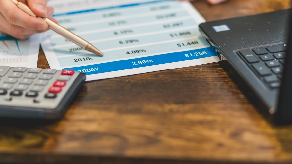 Hands using a pen to review interest-rate figures beside a calculator and laptop.