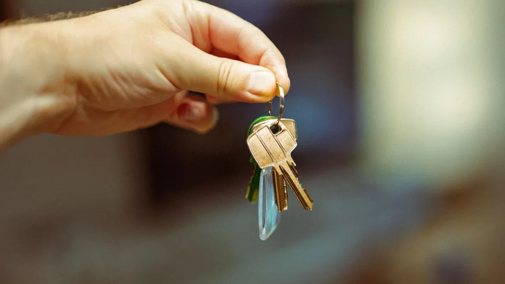A hand holding a set of house keys in a home interior.