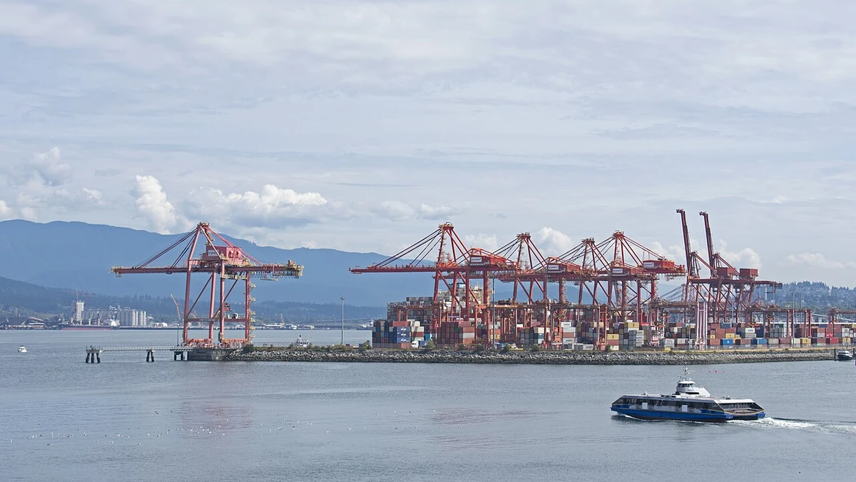 Container cranes and cargo stacks at a Vancouver port terminal, with mountains in the background.