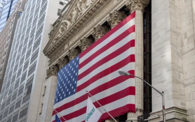 New York Stock Exchange building on Wall Street with a large U.S. flag.