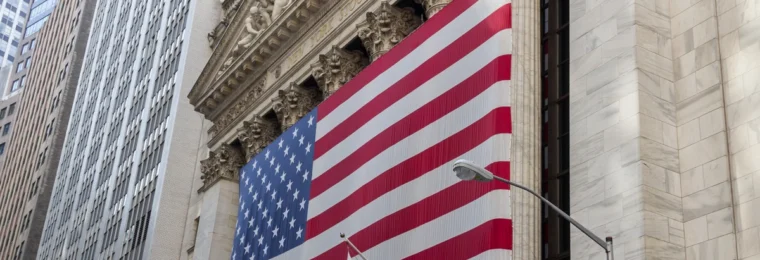New York Stock Exchange building on Wall Street with a large U.S. flag.