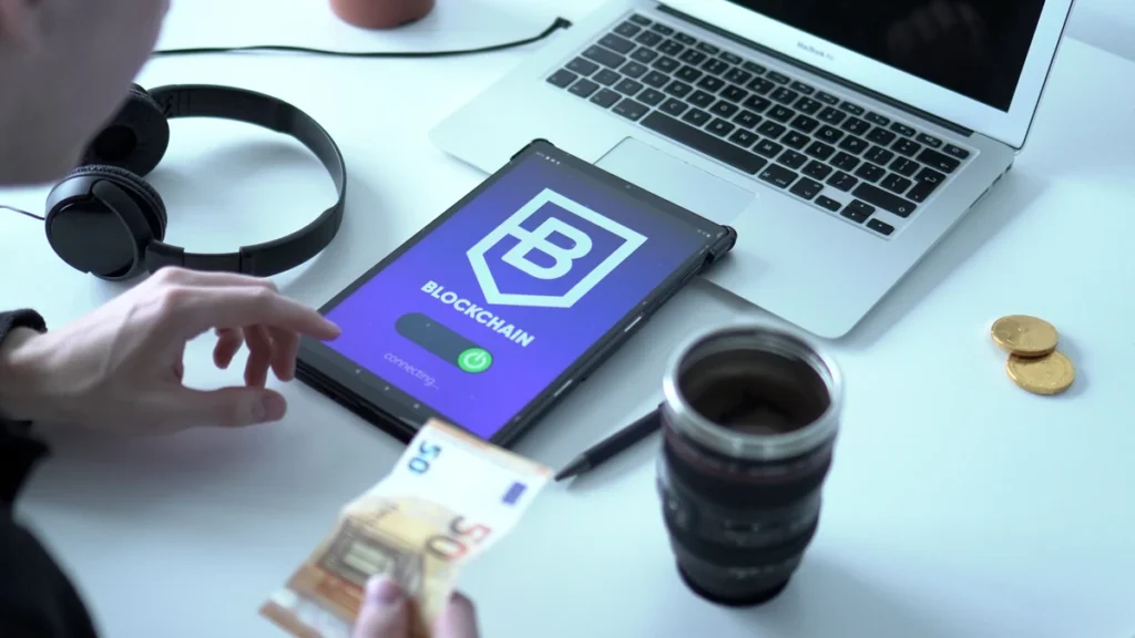 Tablet displaying a blockchain interface beside a laptop and euro banknotes.