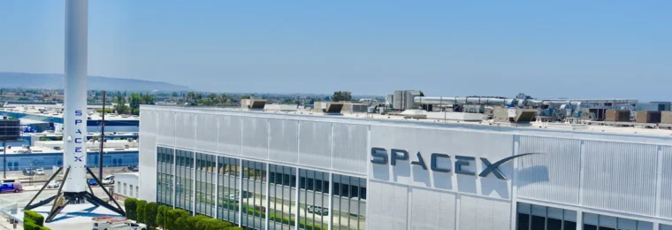 SpaceX factory building in Hawthorne, California, with the SpaceX logo and a Falcon 9 booster outside.