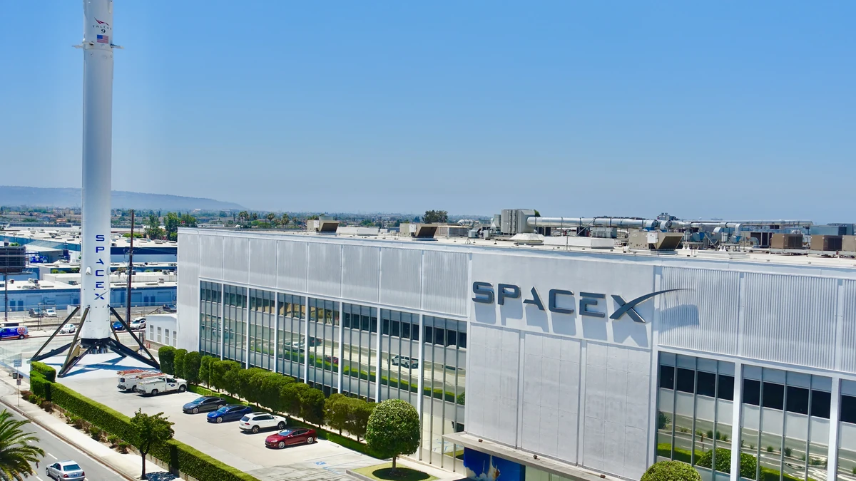 SpaceX factory building in Hawthorne, California, with the SpaceX logo and a Falcon 9 booster outside.