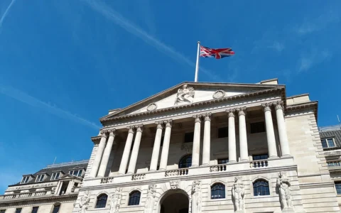 The Bank of England building in London beneath a blue sky with a Union flag flying above it.