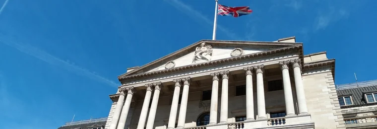The Bank of England building in London beneath a blue sky with a Union flag flying above it.