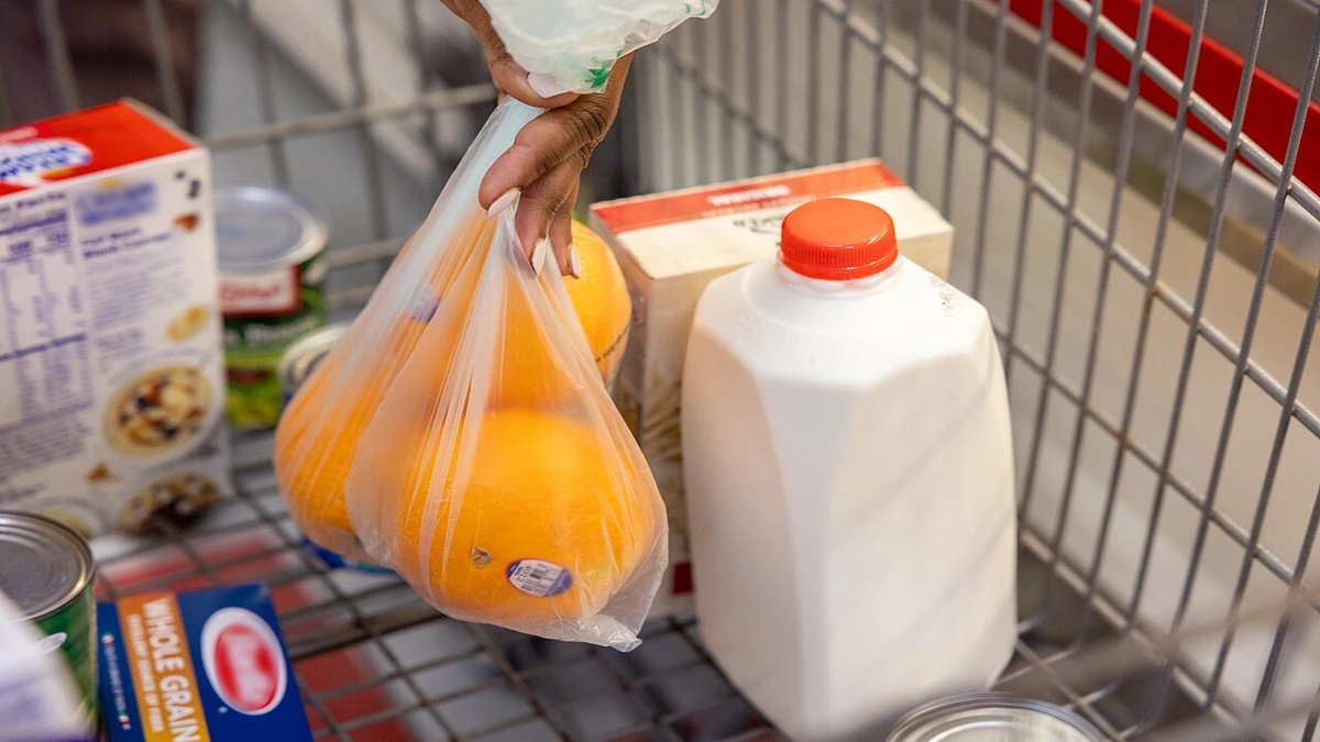 Shopping cart with groceries including oranges, milk, pasta and canned goods.