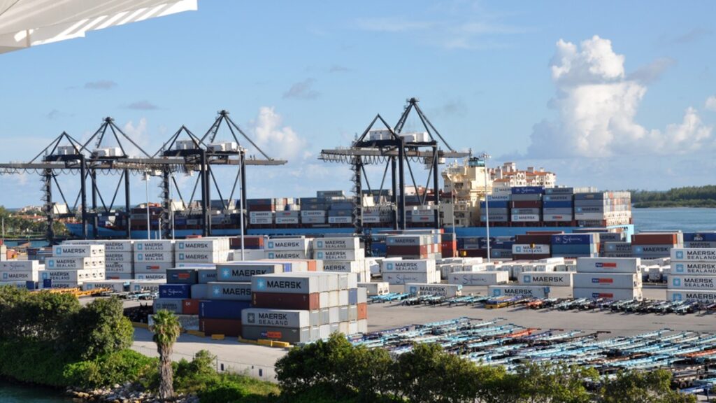 Containers stacked in a shipyard beside a cargo vessel at PortMiami.