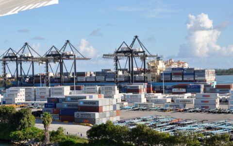 Containers stacked in a shipyard beside a cargo vessel at PortMiami.
