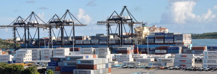 Containers stacked in a shipyard beside a cargo vessel at PortMiami.