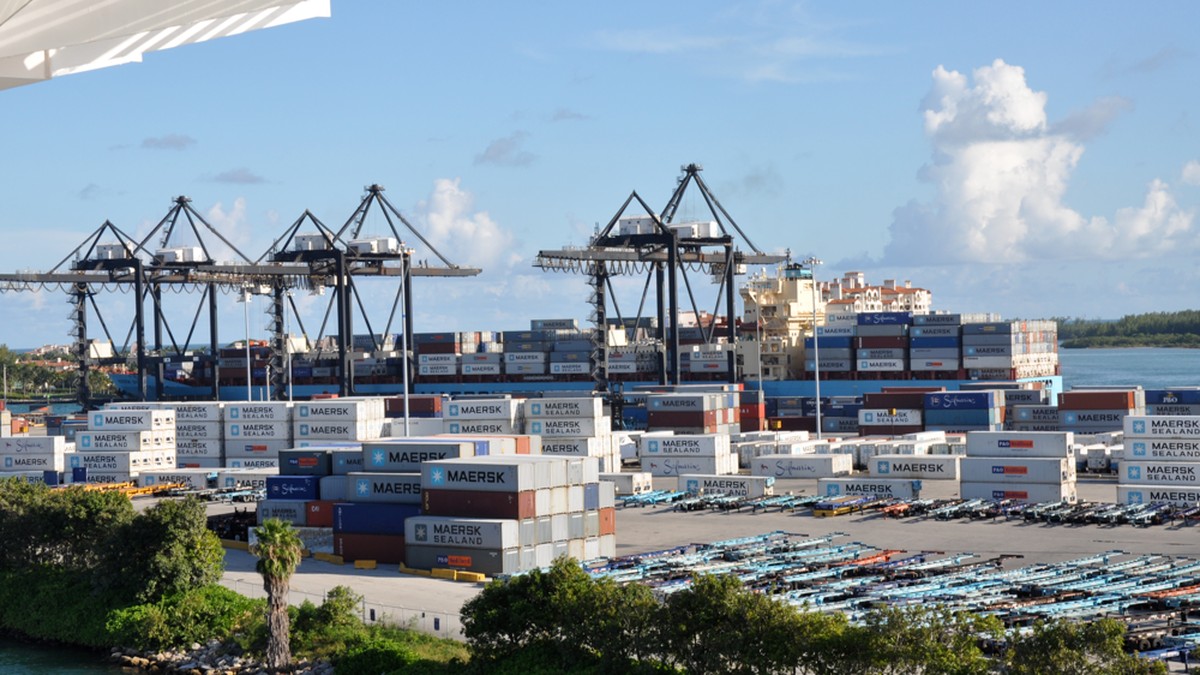 Containers stacked in a shipyard beside a cargo vessel at PortMiami.