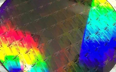 A 300 mm silicon photonics wafer reflecting rainbow colors across patterned chip structures.