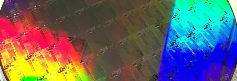 A 300 mm silicon photonics wafer reflecting rainbow colors across patterned chip structures.