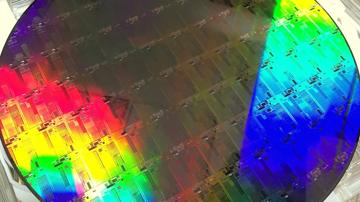 A 300 mm silicon photonics wafer reflecting rainbow colors across patterned chip structures.