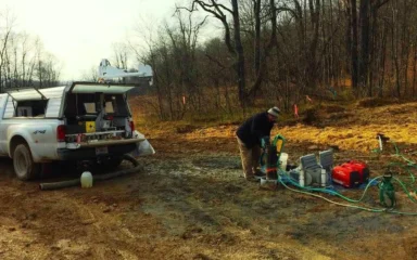 U.S. Geological Survey field worker conducting borehole logging beside a pickup truck and monitoring equipment.