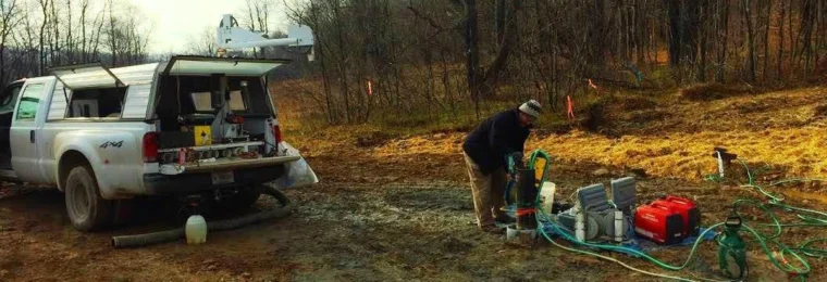U.S. Geological Survey field worker conducting borehole logging beside a pickup truck and monitoring equipment.