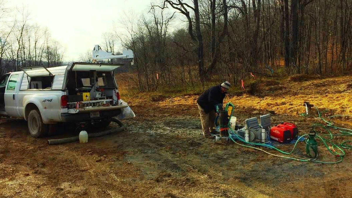 U.S. Geological Survey field worker conducting borehole logging beside a pickup truck and monitoring equipment.