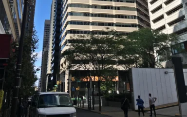Street-level view of 1835 Market Street in Philadelphia, with the office tower, pedestrians and a vehicle visible.