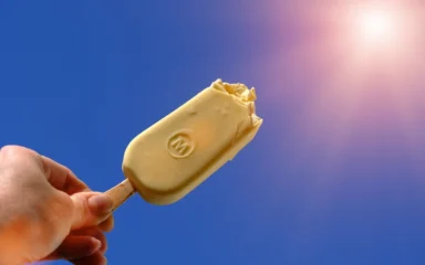 Magnum ice cream bar held against a blue sky near the sun.